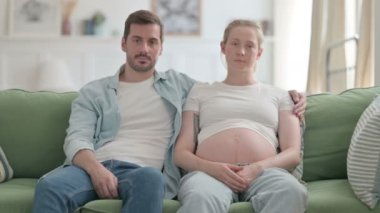 Pregnant Young Woman with Husband Looking at Camera while Holding Her Tummy