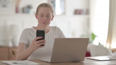 Ofiste dizüstü bilgisayar kullanırken Smartphone kullanan genç kadın 