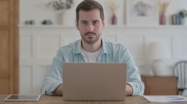 Casual Man Smiling at Camera while using Laptop