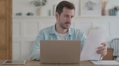 Casual Man Doing Paperwork on Laptop in Office