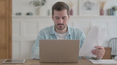 Casual Man Doing Paperwork on Laptop in Office