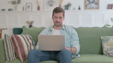Casual Man Thinking while Working on Laptop on Sofa 