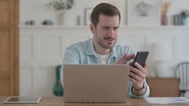 Upset Casual Man Talking Angrily on Smartphone in Office 