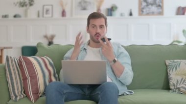 Angry Casual Man with Laptop Talking on Phone on Sofa 