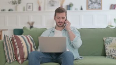 Casual Man with Laptop Talking on Phone on Sofa 