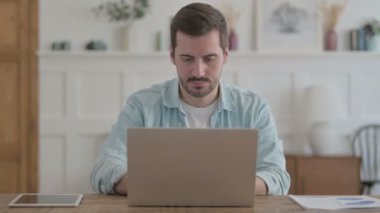 Casual Man Looking at Camera while using Laptop