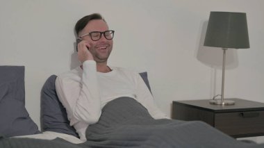 Orta yaşlı adam yatakta Smartphone 'da konuşuyor.