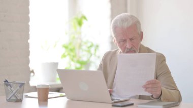 Paperwork by Senior Old Man Working on Laptop in Office