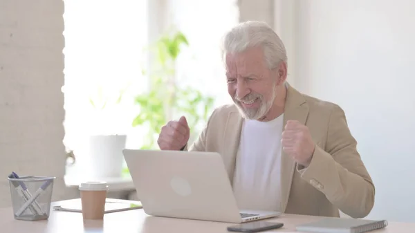 Senior Old Man Celebrating Success while using Laptop in Office