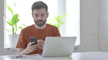 İş yerinde akıllı telefon kullanan yaratıcı genç adam.