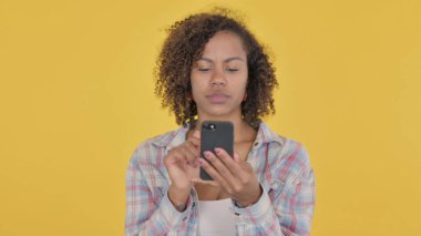 African Woman Browsing Smartphone on Yellow Background