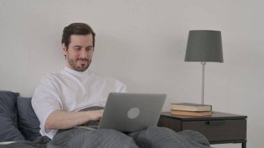 Yatakta dizüstü bilgisayarda çalışan Sakallı Genç Adam.