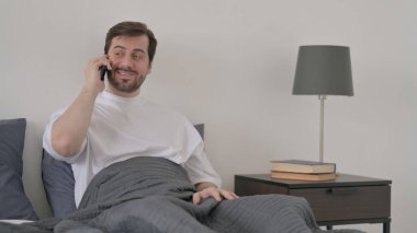 Sakallı Genç Adam Yatakta Akıllı Telefondan Konuşuyor