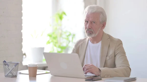 Senior Old Man Shaking Head in Rejection While using Laptop in Office