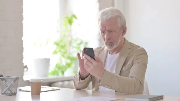 Senior Old Man Browsing Internet on Smartphone in Office