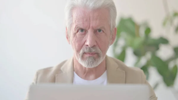 Close Up of Senior Old Man Looking at Camera while using Laptop in Office