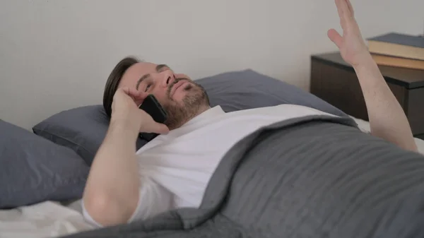 Sakallı Genç Adam Yatakta Uzanırken Telefonda Konuşuyor — Stok fotoğraf