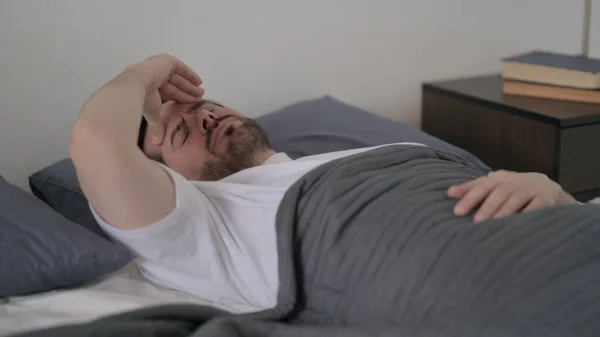 ベッドで寝ている間に頭痛を持っている髭の若者 — ストック写真