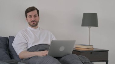 Laptoplu Sakallı Genç Adam Yatakta Kameraya Bakıyor