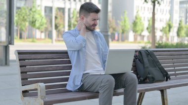 Man with Neck Pain Using Laptop while Sitting on Bench