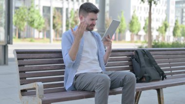 Upset Man Reacting to Loss on Tablet while Sitting on Bench