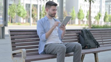 Man using Tablet while Sitting on Bench