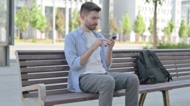 Man Browsing Internet on Smartphone while Sitting on Bench
