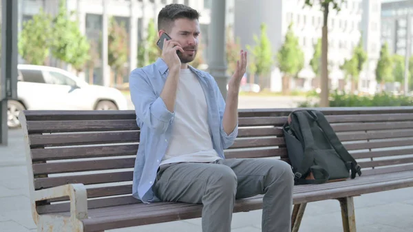 Angry Man Talking on Phone while Sitting on Bench