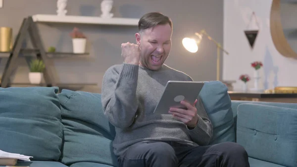Middle Aged Man Celebrating Success on Tablet on Sofa