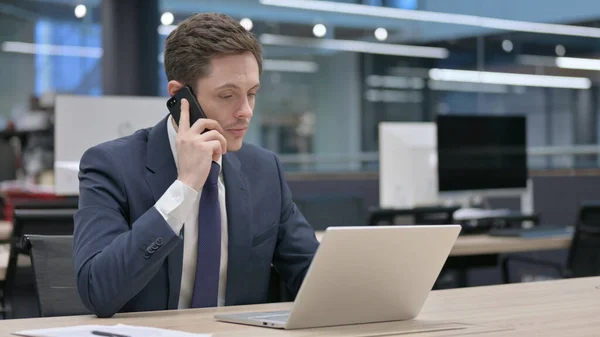 Joven Empresario Hablando Smartphone Mientras Usa Ordenador Portátil Oficina — Foto de Stock
