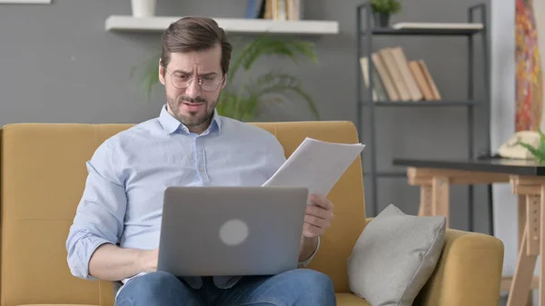 Beard Young Man with Laptop Reacting to Loss on Documents, Sofa