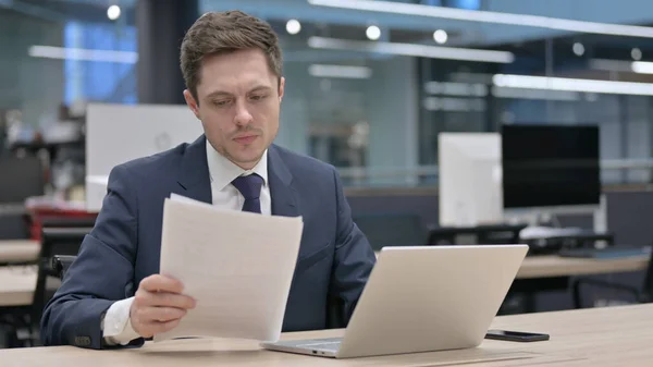 Young Businessman with Laptop Celebrating Success while Reading Documents