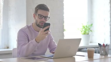 Genç Yetişkin Adam dizüstü bilgisayar kullanırken telefonla konuşuyor