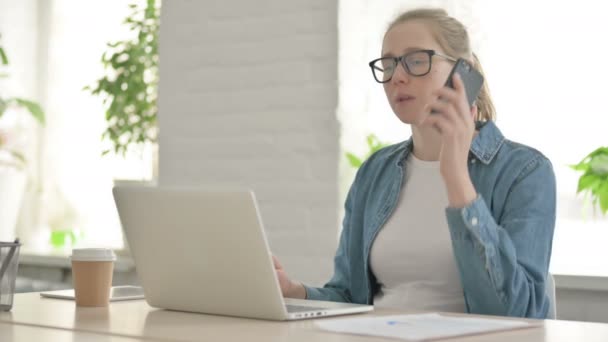 オフィスでノートパソコンを使いながら電話で話す美しい女性 — ストック動画