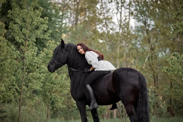 美しい長髪の女の子がフリースラント馬に乗って — ストック写真