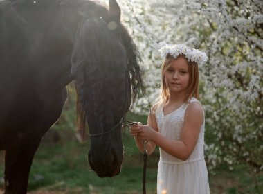 Bahçede bahar çelenginde beyaz saçlı güzel bir kız ve bir Frizya atı.