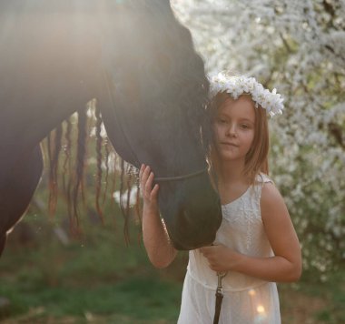 Bahçede bahar çelenginde beyaz saçlı güzel bir kız ve bir Frizya atı.