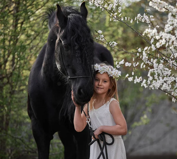 Bahçede bahar çelenginde beyaz saçlı güzel bir kız ve bir Frizya atı.