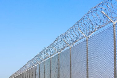 Mavi gökyüzüne karşı dikenli telli sınır çiti