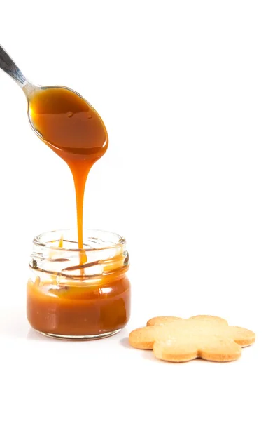 Pouring caramel in a small jar with a spoon with a cookie next t — Stock Photo, Image