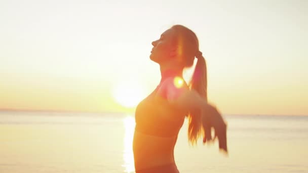 Giovane donna bionda impegnata in yoga sulla spiaggia sullo sfondo del mare dell'alba o del tramonto — Video Stock