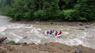 İnsanlar nehirde şişme sallarla baş ediyor. Yağmur yağıyor.