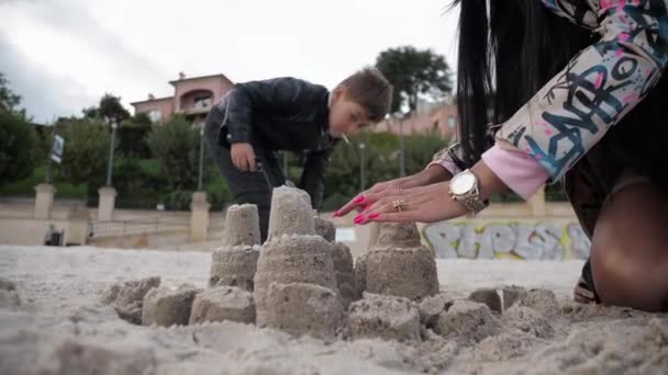 Mama i syn spacerują razem po jesiennej plaży budując zamek z piasku — Wideo stockowe