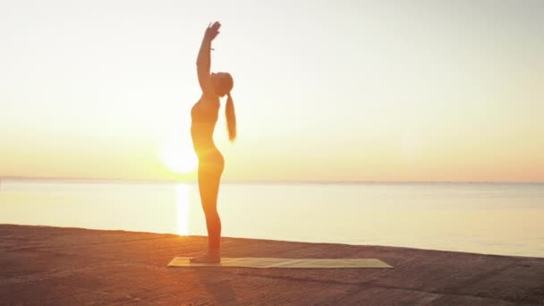 Giovane donna bionda impegnata in yoga sulla spiaggia sullo sfondo del mare dell'alba o del tramonto — Video Stock