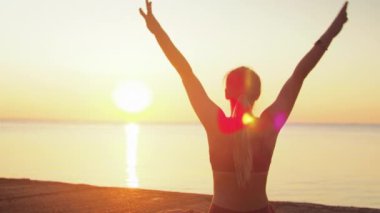 Kumsalda yoga yapan genç sarışın kadın güneşin doğuşunun ya da batışının arka planında