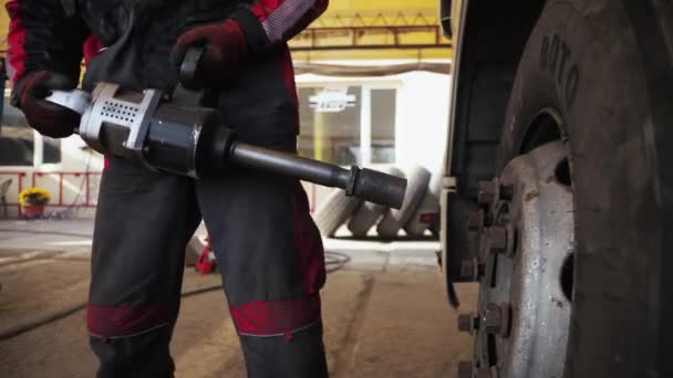 Um homem com a ajuda de uma ferramenta industrial torce os parafusos das rodas de um transporte de mercadorias — Vídeo de Stock