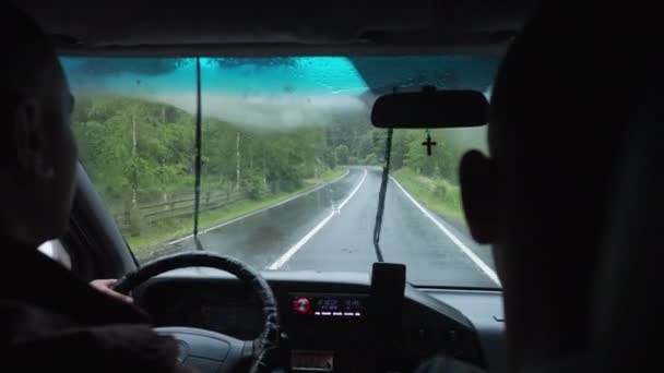 Två unga män rider längs skogen Det regnar på vägen — Stockvideo