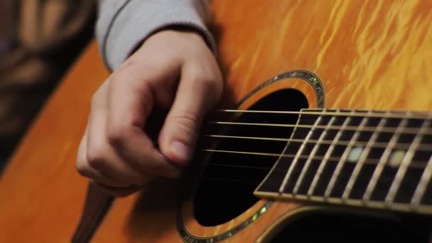 若い男がアコースティックギターの弦と音楽の音を演奏する — ストック動画
