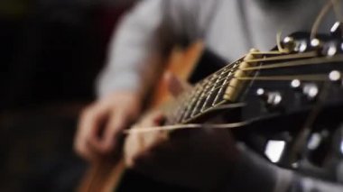 Genç bir adam akustik bir gitarı akort ediyor telleri ve notaları çalıyor