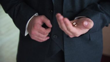 İçerde smokin giyen genç bir adam elinde bir alyans gösteriyor.